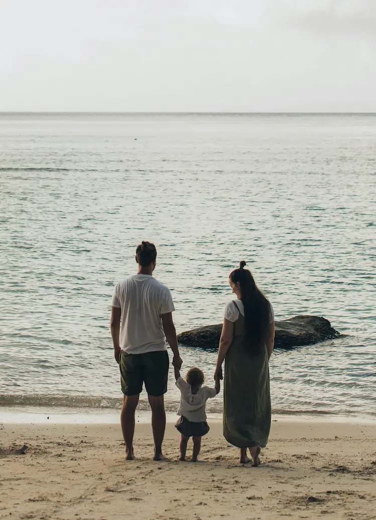 A couple holds hands with their child while standing on a beachfront together